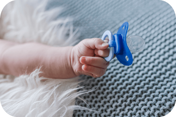 Ein Baby hält einen blauen Schnuller in der Hand.